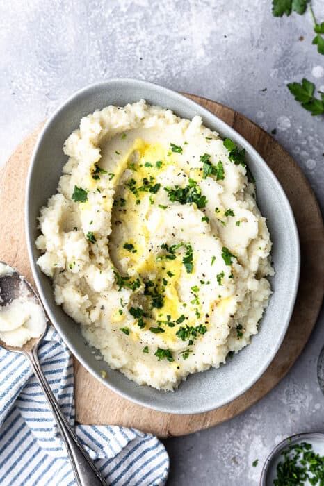 Top view of Whole30 cauliflower mash in a grey bowl on a wooden cutting board