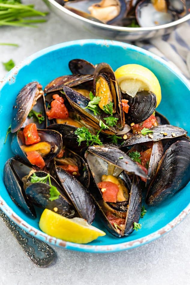 Top view of a serving of Steamed Mediterranean PEI Mussels in a bowl with tomatoes and lemon wedges