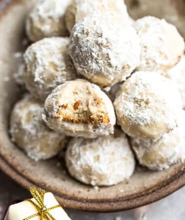 Close up top view of a pile of vegan Mexican Wedding cookies with one Russian tea cake with a bite in a brown bowl