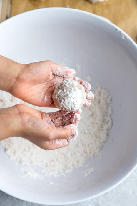 Top view of hands rolling the cookie dough in powdered sugar