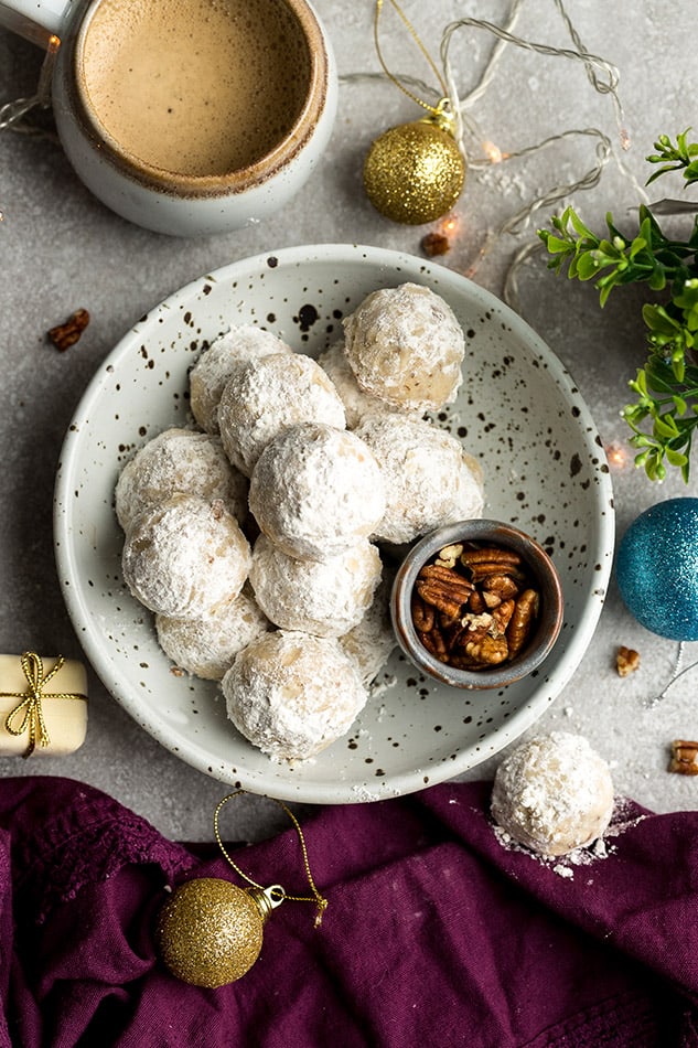 Top view of Mexican Wedding cookies in a white bowl on a grey background with chopped pecans in a small bowl