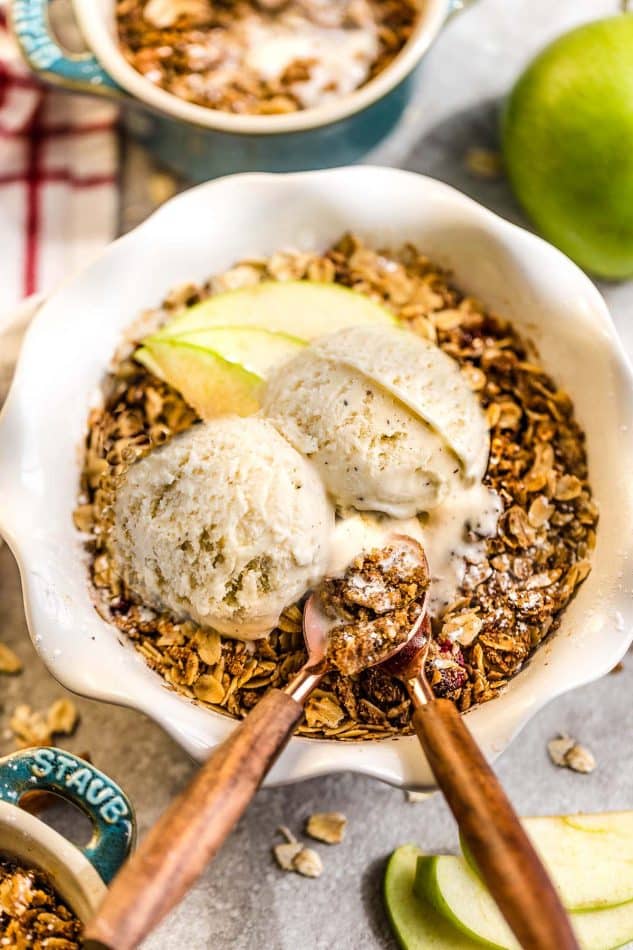 Top view of gluten free apple crisp in white bowl with ice cream and wooden spoons.