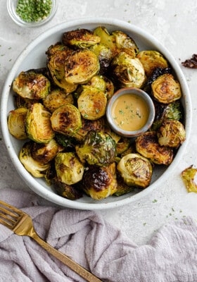 Miso Brussels sprouts in a white bowl with a small bowl of Miso glaze