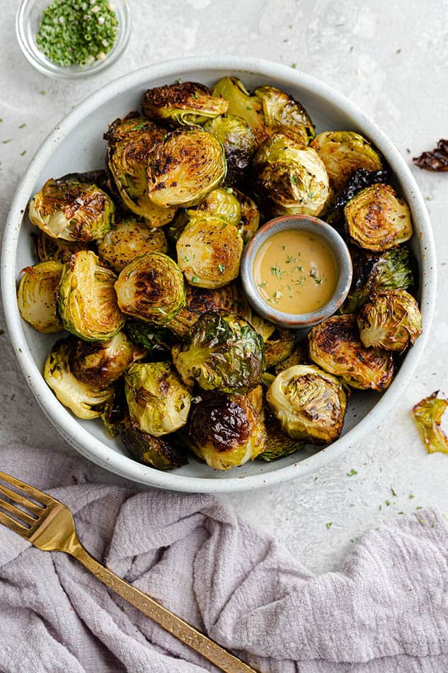 Miso Brussels sprouts in a white bowl with a small bowl of Miso glaze