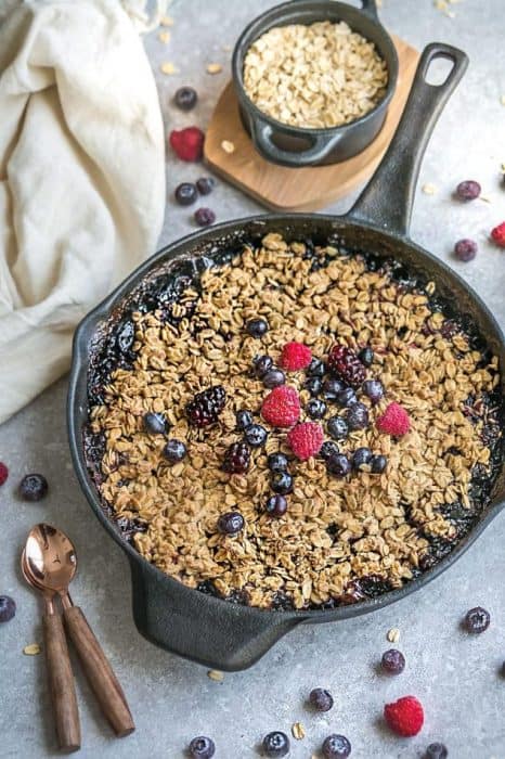 Berry skillet crisp in dark skillet on grey surface with fresh berries and oats.