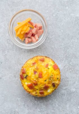 Top view of one muffin tin eggs with ham and cheese on a grey background