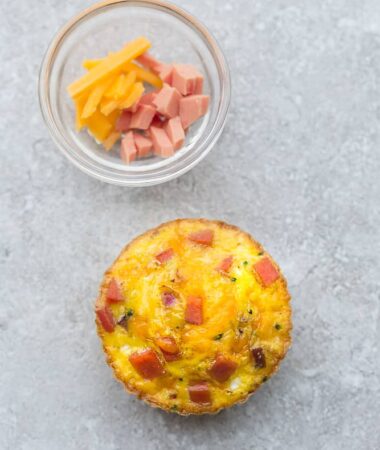 Top view of one muffin tin eggs with ham and cheese on a grey background