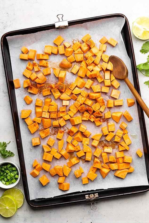 Sweet potato cubes on a lined baking sheet with the seasonings sprinkled on top