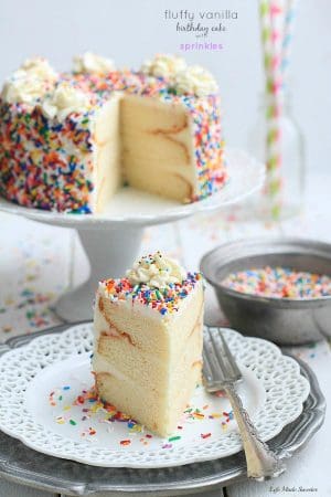 Delicious slice of Fluffy Vanilla Birthday Cake With Sprinkles with a silver fork on a small white serving plate.