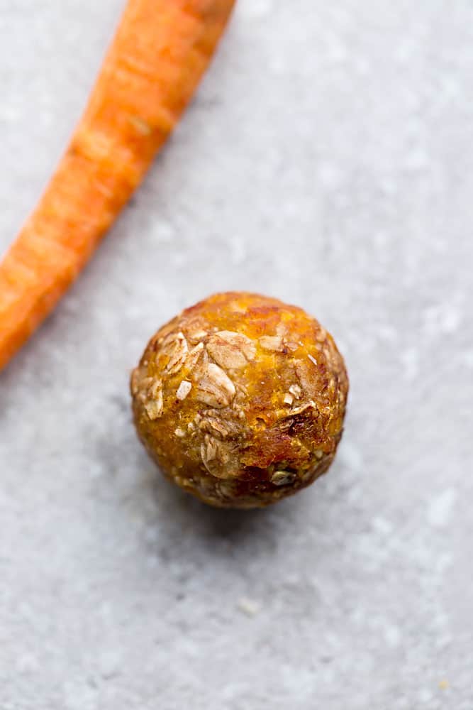 A Carrot Cake Energy Bite on a Granite Surface Next to a Carrot