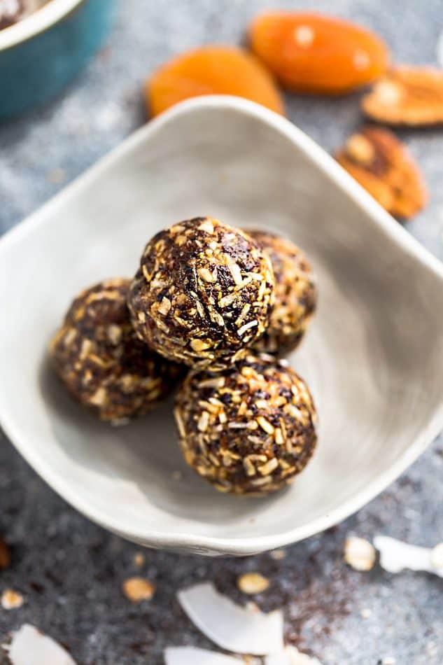 Four Apricot Energy Bites in a small white bowl with sliced apricots on the side. 