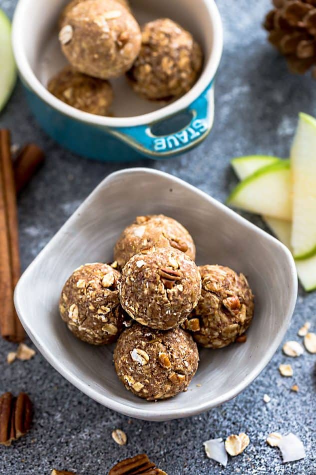 Apple Cinnamon No Bake Energy Balls with oats and pecans in a small white serving bowl on a blue table.