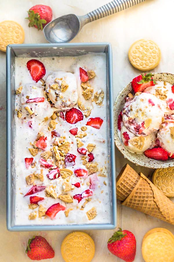 Top view of no churn strawberry shortcake ice cream with cones and fresh strawberries on white surface.