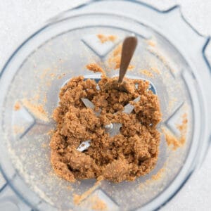 Top view of making nut butter in a Vitamix blender with a spoon on a grey background - gritty texture