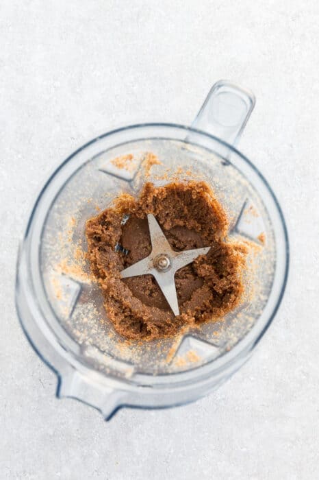 Top view of making nut butter in a Vitamix blender with a spoon on a grey background - pasty texture