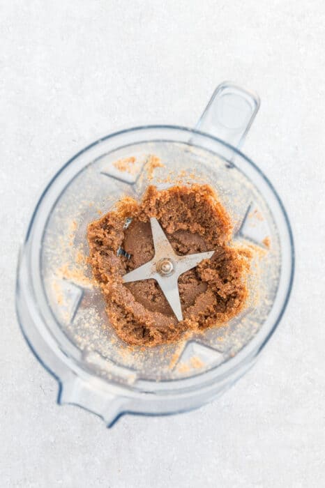 Top view of making nut butter in a Vitamix blender with a spoon on a grey background - sandy texture