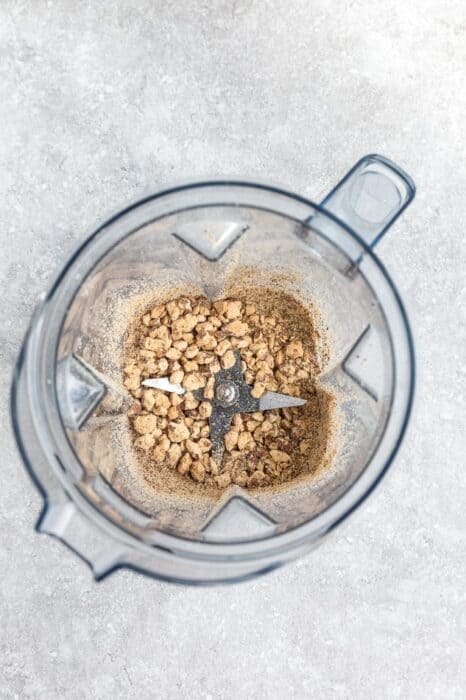 Top view of making nut butter in a Vitamix blender with a spoon on a grey background - crumbly texture