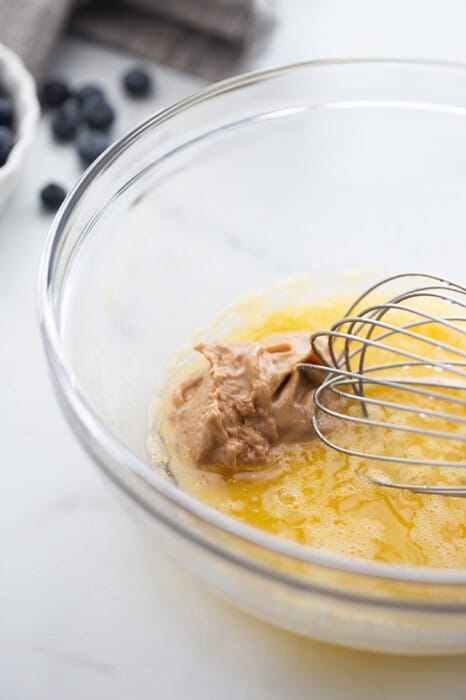 Side view of muffin batter: whisking eggs with almond butter in a clear bowl