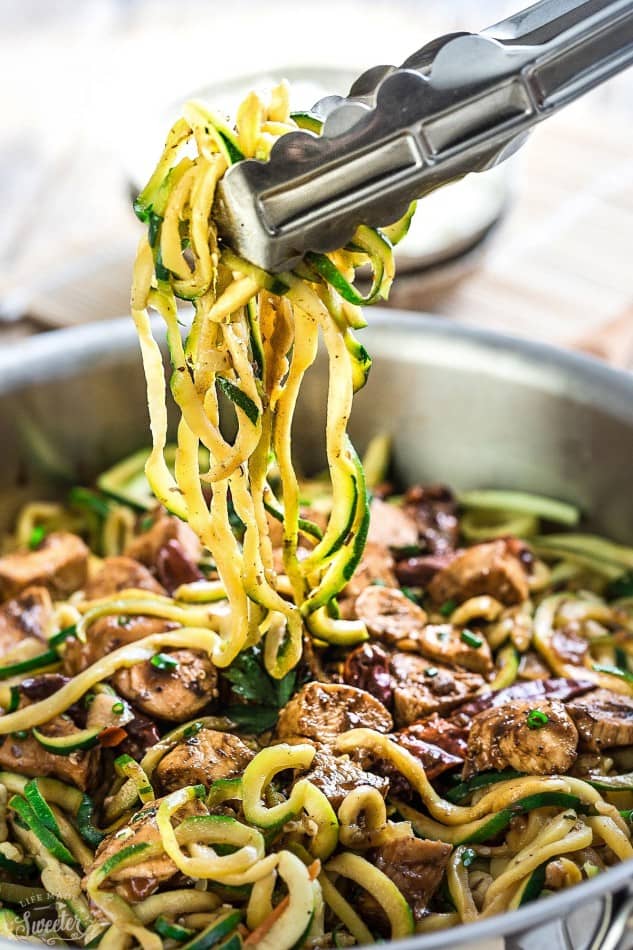 Metal tongs grabbing zoodles from a skillet of Kung Pao Chicken Zoodles {Zucchini Noodles}