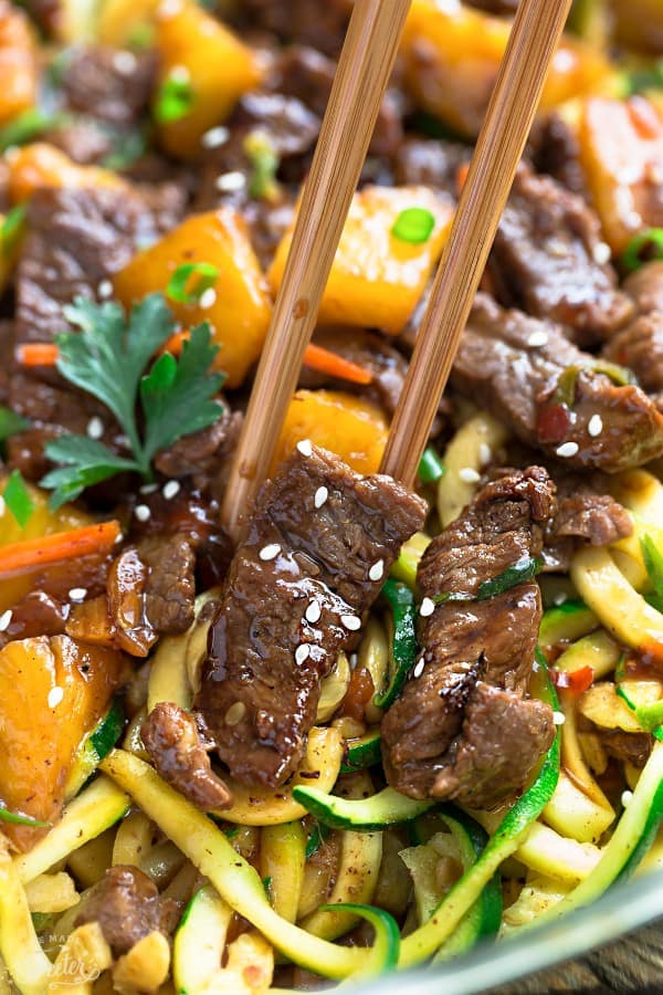 Close-up top view of Mongolian Beef stir fried with zucchini noodles in a stainless steel pan with chopsticks