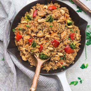 Cashew rice with chicken and vegetables in a white cast-iron pan with a wooden spoon