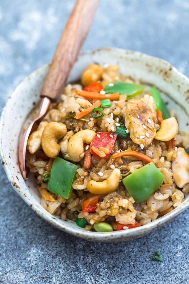 One serving of cashew chicken rice in a beige bowl with a spoon