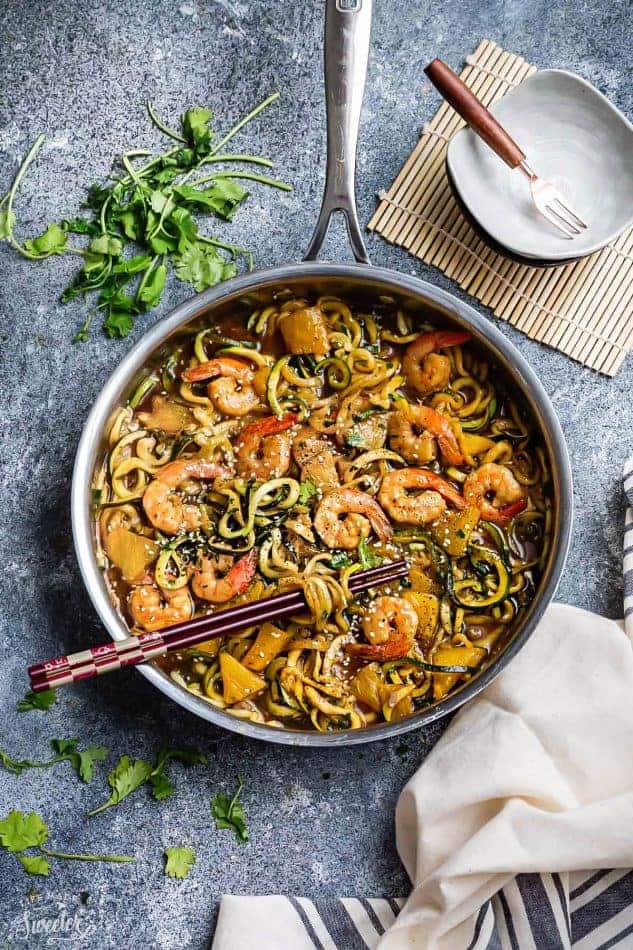 Top view of teriyaki shrimp with zucchini noodles in a stainless steel pan on a grey background with chopsticks