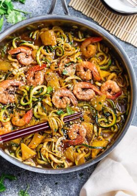 Close-up view of teriyaki shrimp with zucchini noodles in a stainless steel pan with chopsticks
