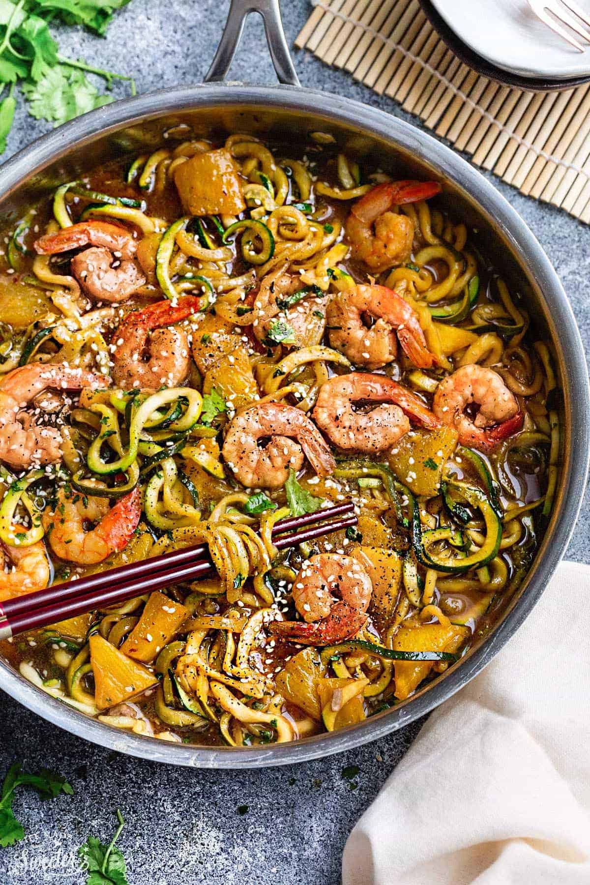 Close-up view of teriyaki shrimp with zucchini noodles in a stainless steel pan with chopsticks