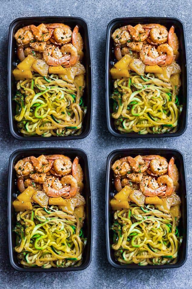 Top view of healthy shrimp teriyaki with zucchini noodles in four black meal prep containers on a grey background