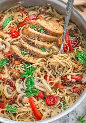 Linguine noodles, chicken, tomatoes and basil in a stainless steel pan with a fork.