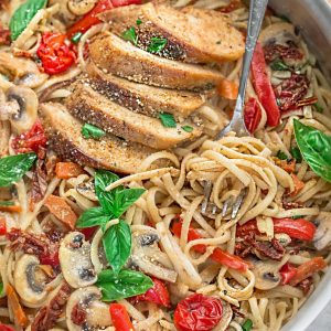 Linguine noodles, chicken, tomatoes and basil in a stainless steel pan with a fork.