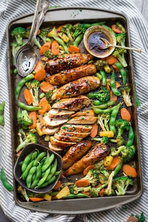 8 baked teriyaki chicken tenders surrounded by vegetables and homemade teriyaki sauce on a baking sheet