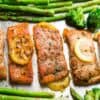 Roasted salmon fillets on a baking sheet with lemon slices and roasted veggies