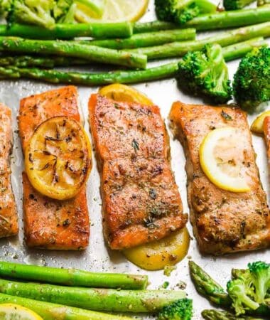 Top view of oven baked salmon on a baking sheet with asparagus and lemon