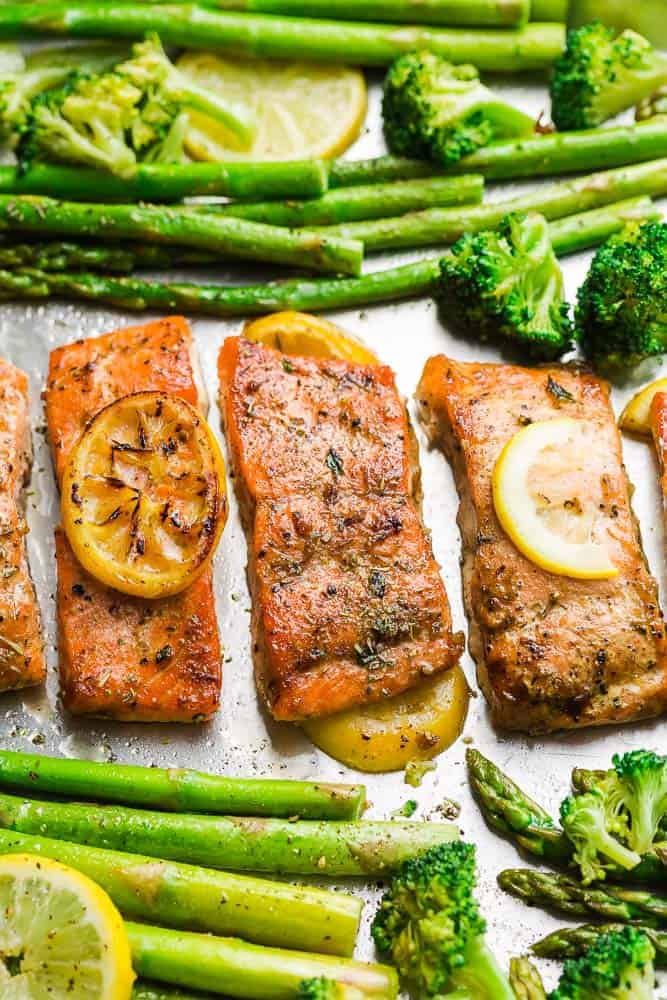 Roasted salmon fillets on a baking sheet with lemon slices and roasted veggies