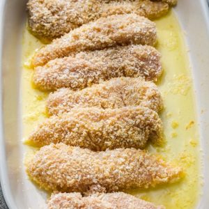 Top view of breaded chicken pieces in a baking dish with melted butter