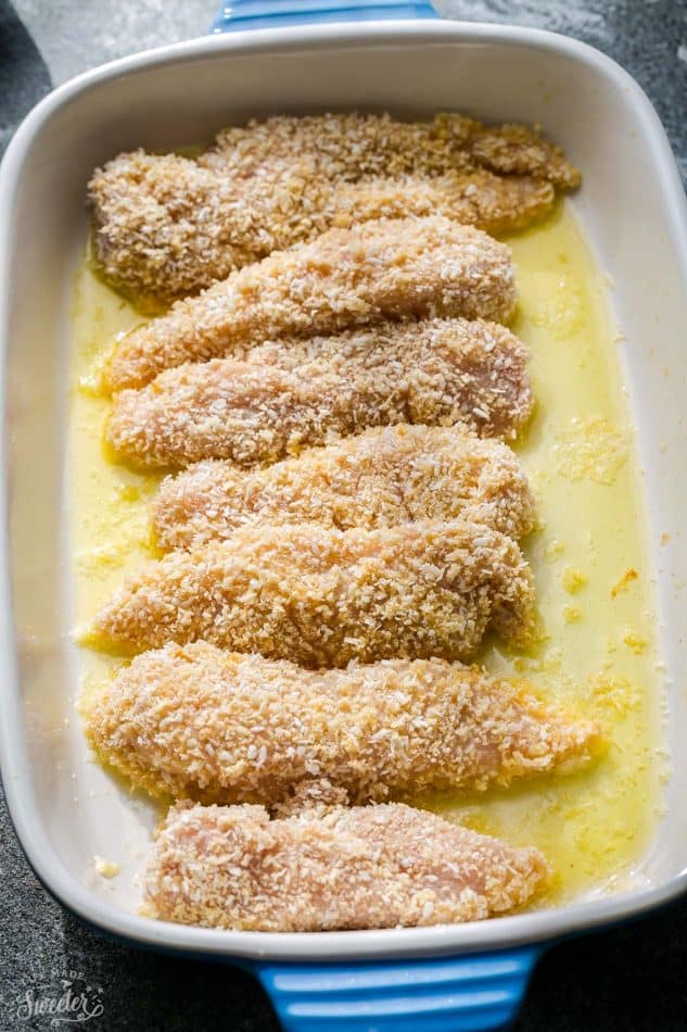 Breaded raw chicken pieces in a baking dish with melted butter