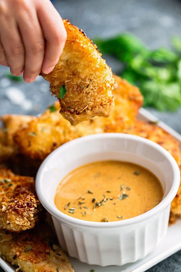 A Chicken Tender Being Held Over a Ramekin of Dipping Sauce