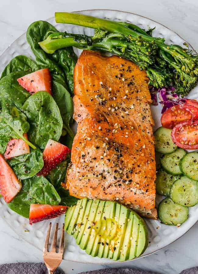 Baked salmon in a bowl with a strawberry spinach salad beside it