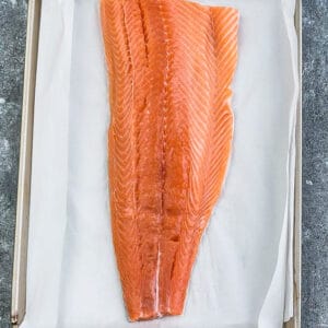 Raw salmon on a baking sheet with a parchment paper lining