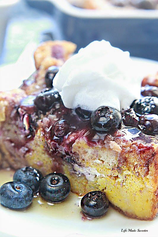 A close-up shot of a slice of blueberry breakfast casserole topped with a dollop of whipped cream