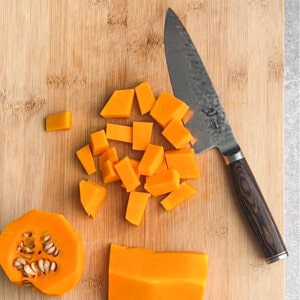 Cubes of butternut squash on a cutting board beside a sharp chef's knife