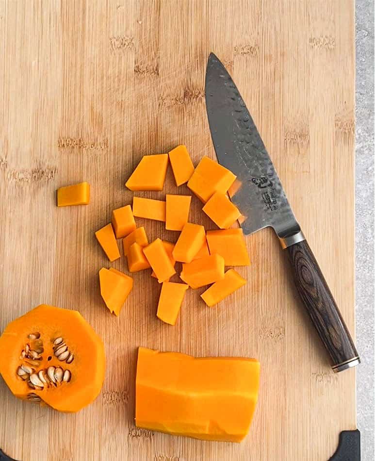 Cubes of butternut squash on a cutting board beside a sharp chef's knife