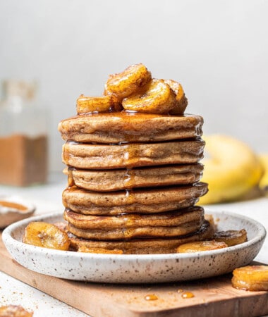 Gluten-free pancakes piled onto a speckled plate on top of a small wooden cutting board