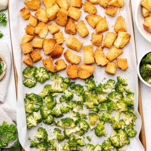 Toasted broccoli florets and sour dough chunks on a parchment lined baking sheet