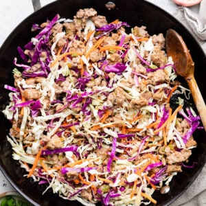 Sautéed green and red cabbage, shredded carrots and ground turkey in a black wok with a wooden spoon