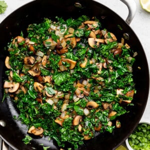 Diced mushrooms, onions and shredded kale inside of a cast-iron skillet with a metal handle