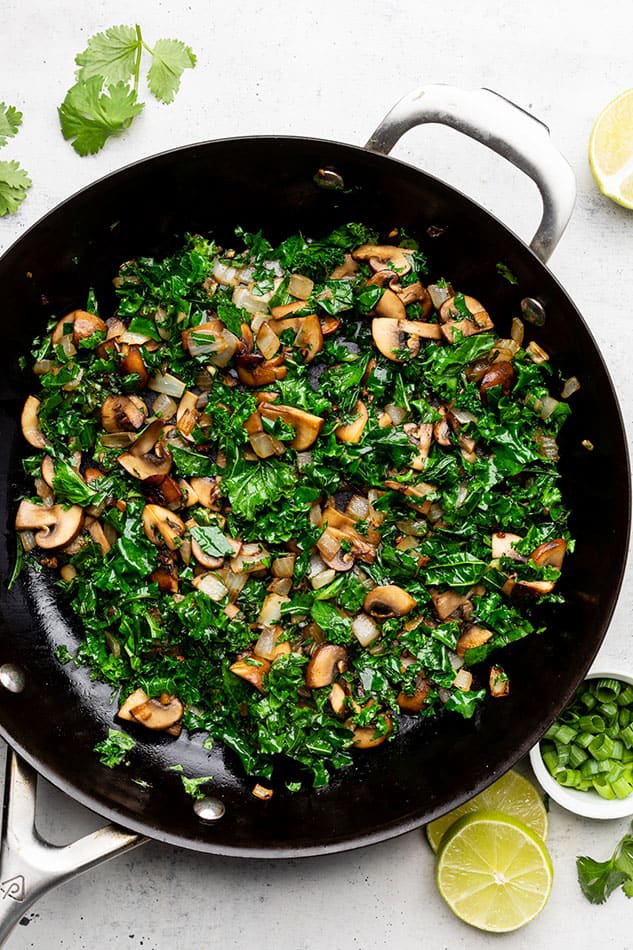 Diced mushrooms, onions and shredded kale inside of a cast-iron skillet with a metal handle