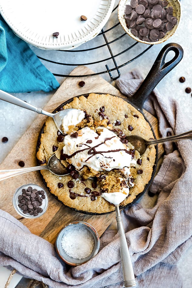 Top view of skillet cookie with four spoons and chocolate chips.